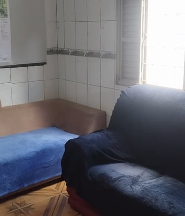 Small living room with tiled walls featuring a blue sofa and a tan daybed couch by a window.