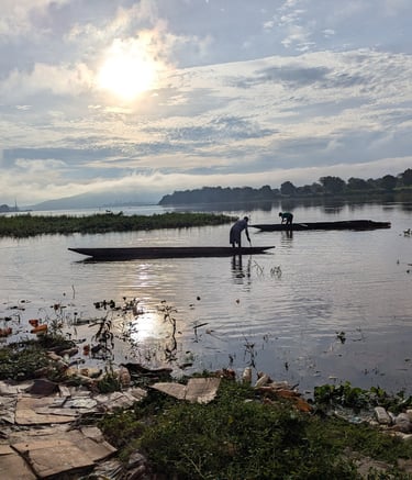 Fishermen in wooden dugout canoes on a river during a bright sunrise with plastic pollution in the foreground.