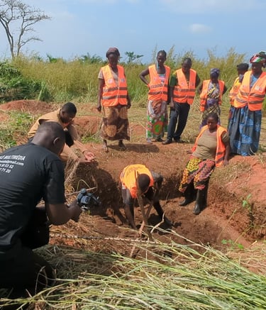 Agricultural workers in safety vests dig a trench in a field while a videographer records the manual labor.