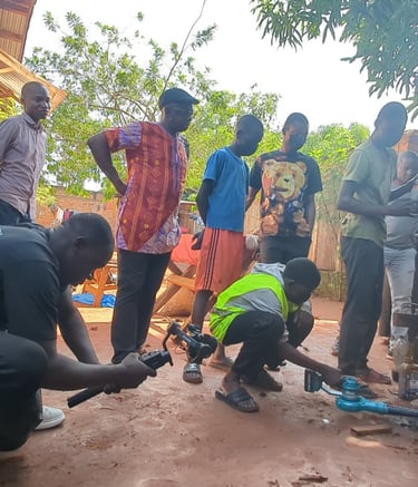 A film crew records a community vocational training session outdoors using a gimbal and professional camera equipment.