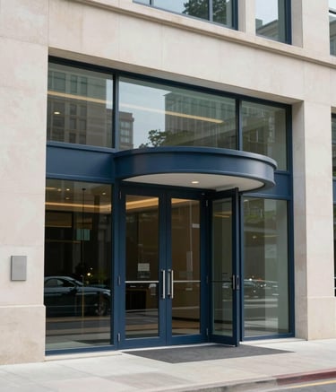 A professional architectural photograph of a sleek, modern glass door entrance at a large North American corporate headquarters. The lighting is bright and clean, emphasizing the off-white stone and dark blue metal frames.