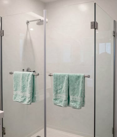 A stunning transformation photo of a modern bathroom in a North American home, featuring a large glass-enclosed shower with pristine white tiling and soft mint green towels hanging neatly on a sleek chrome rack.
