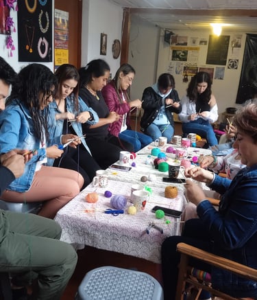 Personas concentradas al rededor de una mesa con hilos, herramientas y bebidas calientes, elaborando mandalas tejidos