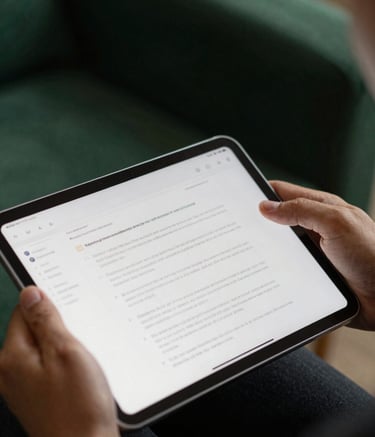 A focused close-up photograph of a person's hands holding a digital tablet displaying a structured document. The lighting is soft and professional, highlighting a sense of study and preparation. The background features a blurred room with deep forest green and charcoal tones, emphasizing a grounded and serious environment.