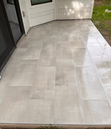 Modern outdoor patio with large grey porcelain tiles installed next to a sliding glass door.