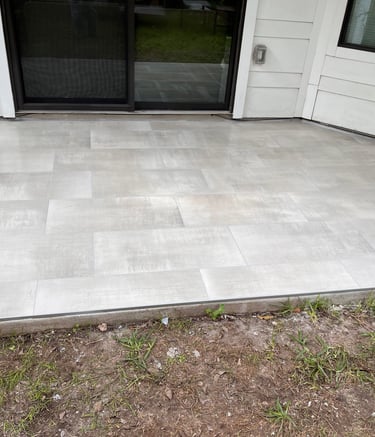 Modern outdoor patio featuring light gray porcelain pavers installed next to a sliding glass door.