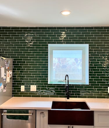 Modern kitchen featuring a dark green subway tile backsplash and a black farmhouse sink with white countertops.