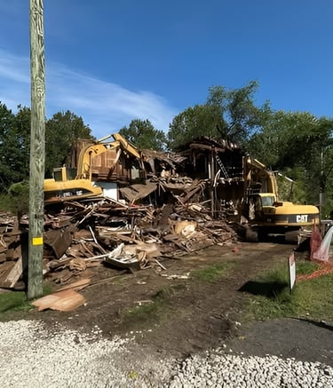 Yellow Cat excavators demolishing a wooden residential building on a construction site.