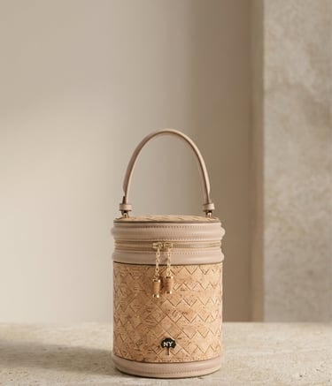 Elegant cylinder cork handbag with a top handle and gold zipper detail on a stone surface.