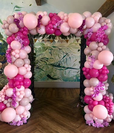 Elegant pink and magenta balloon arch with floral accents for a party entrance or event decoration.