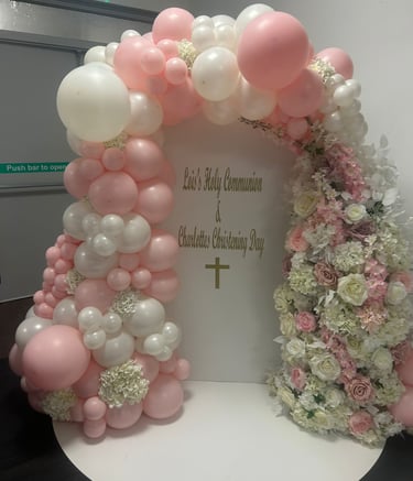 Elegant pink and white balloon arch with floral decorations for a Holy Communion and Christening event.