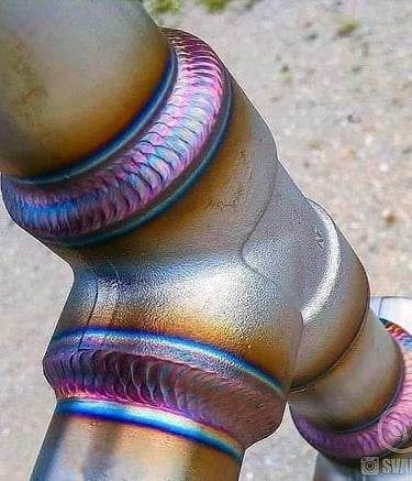 Precision TIG welding on a titanium pipe joint with colorful heat tint and clean stack of beads.