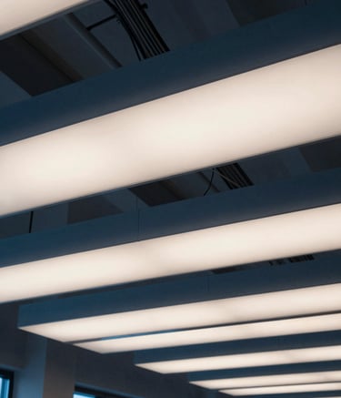 Photography of a modern office building interior in Poland, showing professionally installed architectural ceiling lighting and visible, neatly routed cable trays. The lighting is soft and neutral. The aesthetic is professional and modern, featuring colors like Dark Blue and Off-White.