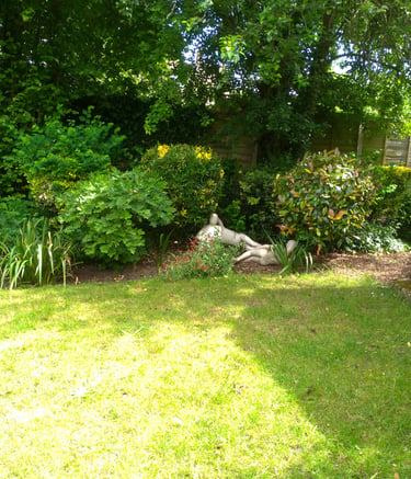 Backyard garden with green lawn, lush bushes, and stone statues next to a green shed.