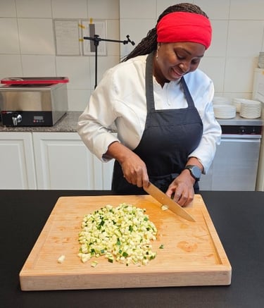 Chef Viviane in white chef jacket and black apron chopping vegetables on a bamboo board in a professional kitchen