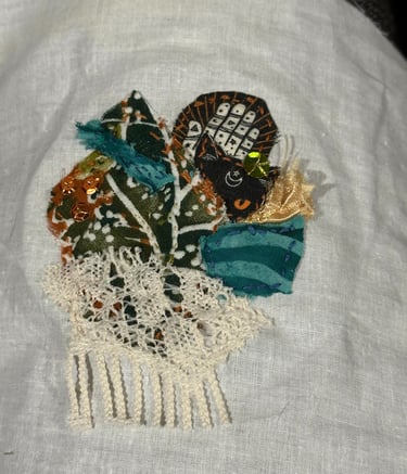 fabric collage with sequins in shades of green, teal, rust, black and cream; cat face and lace used
