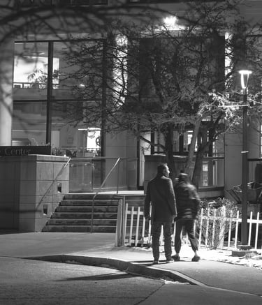 Black and White Photo of a couple walking at night below the glow of a street lamp.