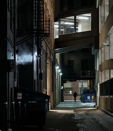 Moody and cinematic image of a silhouetted man walking down a city alley at night. 