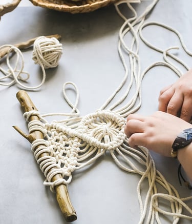 mujer realizando macrame decorativo sobre una rama de madera