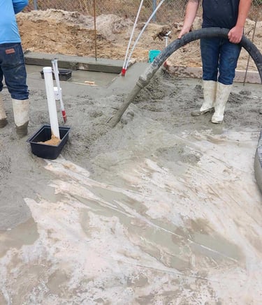 Two workers in white boots pumping concrete for slab.