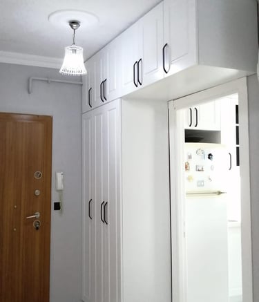 Beyaz portmanto, vestiyer ve üzerinde siyah kulplarla birlikte ayna kapaklı dolap.
