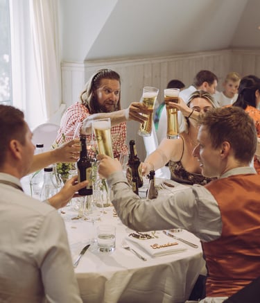 Hochzeitsgäste stoßen fröhlich mit Biergläsern am Tisch an. Authentische Eventfotografie von Just Perspectives.