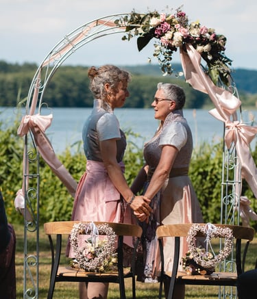 Zwei Bräute halten sich bei der freien Trauung unter einem Blumenbogen an den Händen. Foto: Joel Pingel.