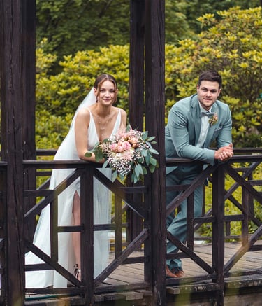 Brautpaar lehnt entspannt an einer Holzbrücke im Grünen. Hochzeitsportrait von Just Perspectives.