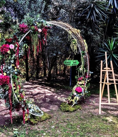 A large circular arch decorated with vibrant pink and red flowers and lush greenery in a garden setting