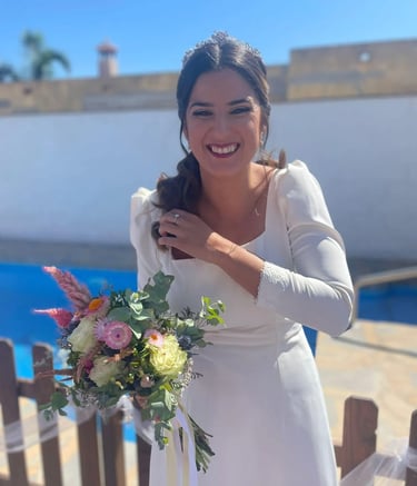 A happy bride in a white wedding dress, smiling and holding a colorful flower bouquet