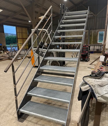 Industrial galvanized steel staircase with non-slip grating treads and metal handrails in a workshop.