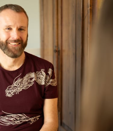 A man wearing a dark red t shirt with dragon imagery is sitting coaching a client