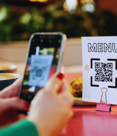Um cliente usa seu smartphone para escanear um código QR no cardápio enquanto está sentado à mesa do