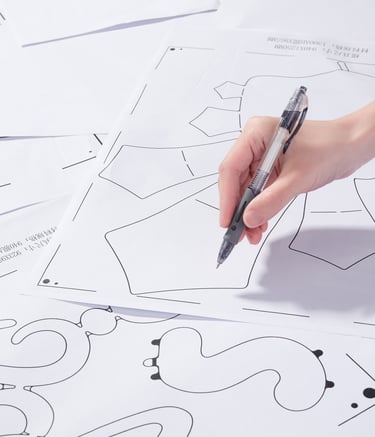 A person using a black ink pen to trace a garment sewing pattern on white paper.