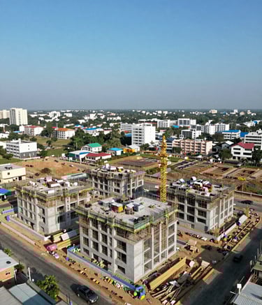 A wide-angle aerial drone photograph of a modern residential construction project in a South Asian / Indian urban area. The sky is a clear sky blue, and the building structures show organized progress under a professional construction management protocol.