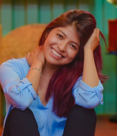 A smiling young woman with auburn hair wearing a blue blouse posing indoors.