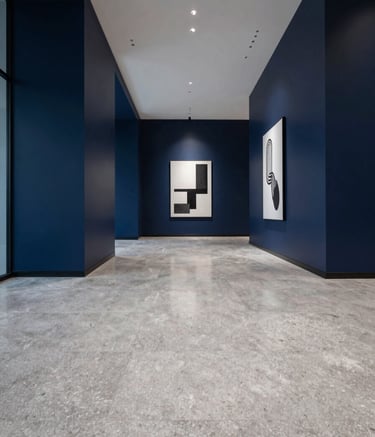 A wide-angle photograph of a minimalist, high-end corporate office lobby. The floor is polished pearl grey stone. Walls are a deep navy blue with subtle lighting. The atmosphere is sophisticated and quiet, with sharp geometric lines and a single piece of modern art.