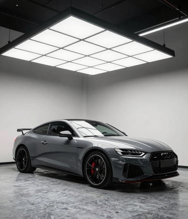 A high-end automotive detailing studio in North American / US, featuring a sleek modern car under professional LED panel lighting. The setting is clean with slate grey flooring and off-white walls, emphasizing a premium and performance-oriented atmosphere.
