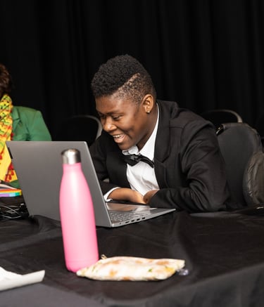 A mixed-race person in green, and black woman in a manual wheelchair sit at a table