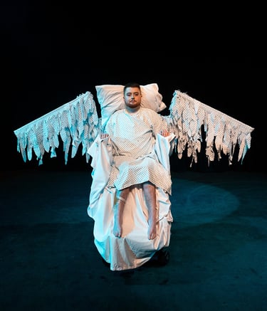 An electric wheelchair user in a hospital gown, with swooping wings made of the same fabric
