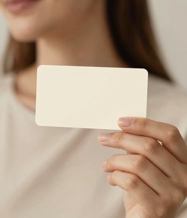 A serene close-up of a person with radiant, healthy-looking skin holding a delicate cream-colored contact card. The lighting is soft and warm, reflecting a gentle glow. Background features soft-focus textures of #FDF8F0 and #E4D5C5.