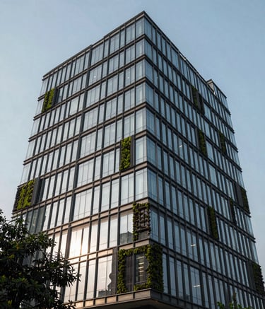 Photography of a contemporary commercial building facade in the Delhi Mohan Cooperative area. The architecture is modern with glass and steel, reflecting the sky. Touches of dark moss green landscaping are visible, creating a professional and high-end atmosphere.