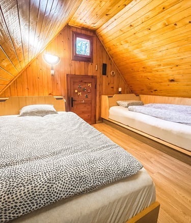 Cozy attic bedroom with two twin beds under a sloped wooden plank ceiling and walls.