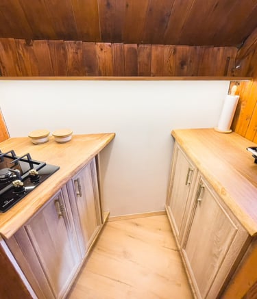 Rustic cabin kitchen featuring a gas stovetop, wood countertops, and light oak cabinets.