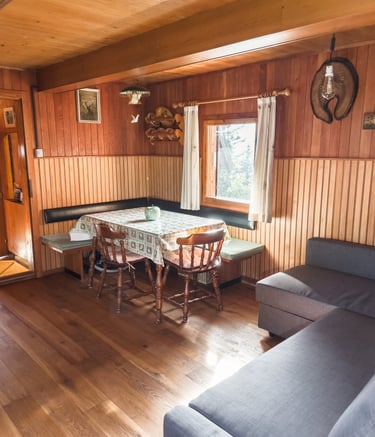 Rustic log cabin interior with wood paneled walls, a dining table with chairs, and a grey sofa.