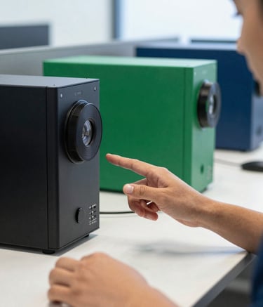 A sharp, close-up photograph of a professional in a modern North American / US office setting interacting with high-end tech hardware. The environment is bright and clean with accents of emerald green and dark blue in the background, conveying a sophisticated and high-tech atmosphere.
