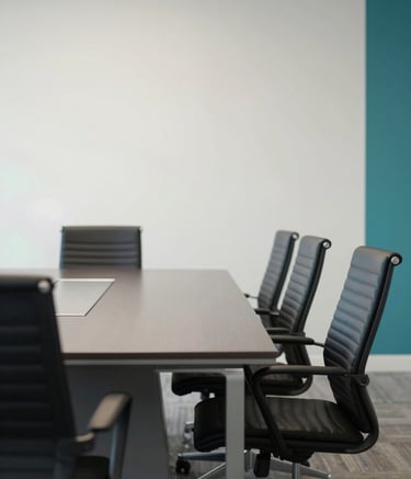 Photography of a modern, professional boardroom in North American / US, featuring a polished dark gray table and ergonomic chairs against a soft off-white wall with minimalist teal accents, bright natural light.