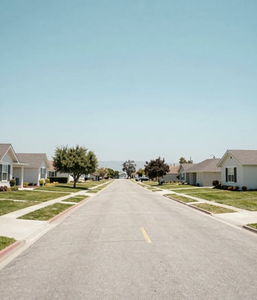A wide-angle landscape photography shot of a quiet and clean North American / US suburban street in Lemoore, California. The atmosphere is peaceful and bright under a clear sky, featuring homes with manicured lawns. The color palette incorporates soft sky blue and off-white, reflecting a sense of safety and professional care.