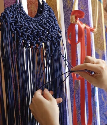 Una mujer elabora de manera artesanal un collar de macramé