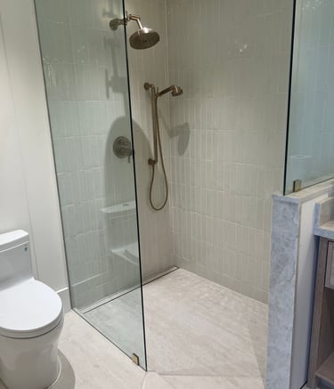 Modern walk-in glass shower featuring vertical subway tiles and elegant gold hardware fixtures.